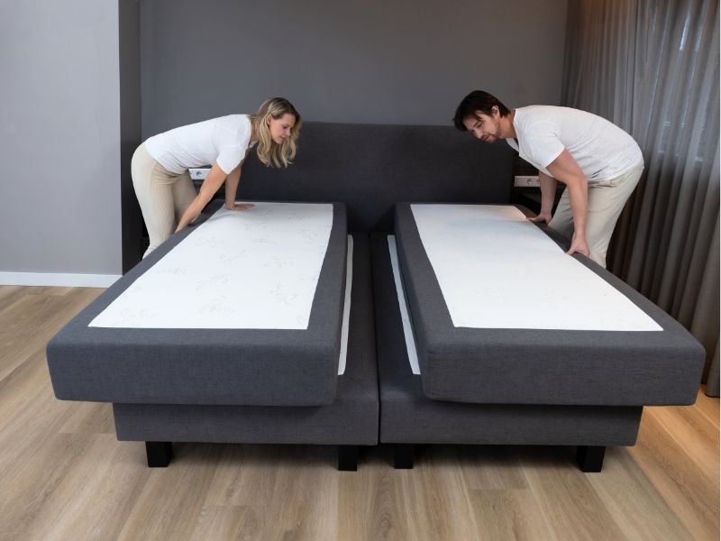 Two mattresses being pushed together by hand to close the gap