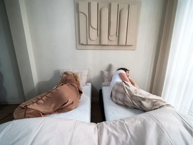 Stel ligt met de ruggen naar elkaar op twee losse bedden met een spleet ertussen